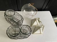 Two wire baskets each holding two clear glass containers and one hanging glass globe with twine on a table.