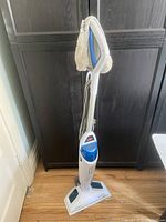 Full view of the Bissell PowerFresh Steam Cleaner standing upright with the bonnet attached, showing its white and blue body and attached cord.