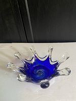 Front side view of cobalt blue and clear glass bowl showing eight elongated finger-like extensions and swirling center.