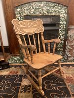 Front view of child's wooden rocking chair with carved sunrise pattern back and curved rockers on carpeted floor.