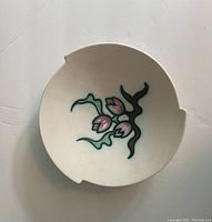 Top view of round decorative plate with stylized pink tulip design and green stems, off-white background, showing two notches on rim.