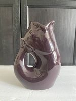 Front view of a glossy merlot-colored fish-shaped ceramic pitcher with a hollow center and a large spout tail.