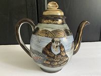 Side view of ceramic teapot showing hand-painted portrait, gold floral embellishments, and a dragon motif along the body and spout. Lid shows wear and rough edges.