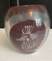 Front view of the purple-tinted rounded glass vase with white stylized bird engraving.