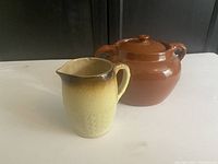 Photo of both Redcliffe Alberta Pottery pieces on white surface showing jug with chip on rim and brown covered casserole.