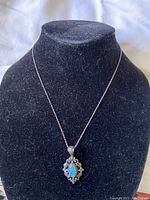 Front-left view of the silver chain necklace with pendant, displayed on black velvet stand
