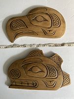 Top side view of two wooden carvings, one an Eagle and the other a Killer Whale, placed side by side with measurement tape showing their approximate widths of 12 inches.