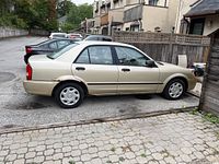 Side view of gold 2001 Mazda Protegé sedan showing overall exterior and rust on rear fender