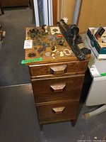 Photo showing the vintage wooden three-drawer cabinet with assorted metal hardware and figurines on top