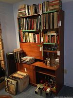 Full view of the wooden cabinet/bookcase filled with books and decorative items, showing the top shelving and lower cabinet with sliding doors.
