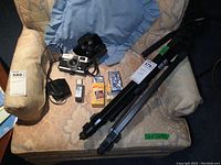 Full lot displayed on armchair including Canon camera, tripod, film cartridges, light meter, and camera case.