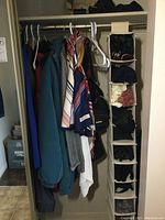 Closet showing ladies jackets, scarves, and hanging clothes with hanging organizer containing gloves, hats, purse, and umbrella