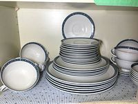 Photo showing stacked dinner plates, salad plates, soup bowls, saucers, and coffee cups with blue Moonstone pattern.