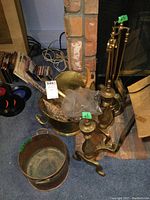 Brass fireplace tools, andirons, copper basket and brass coal scuttle arranged together beside fireplace.