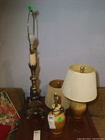 Photo showing three lamps together: two smaller ceramic base lamps with shades and one tall ornate metal base lamp without a shade.