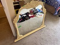 Front view of the large vintage mirror leaning against a wall showing decorative wooden frame and mirror surface.