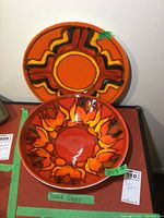 Photo of the two Poole Pottery pieces: a bowl and platter, showing the bowl's floral colored design and the platter's geometric pattern against a white wall background.