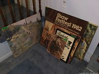 Photo showing all five prints and posters arranged upright on the floor, including the large Shaw Festival poster and other assorted art pieces