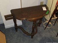 Side view of wooden three-legged demi-lune side table showing marks and scratches on surface, carved legs and stretcher base.