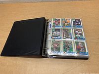 Black three-ring binder containing plastic sleeves with 1989 Topps football cards, showing multiple player cards with blue and green bordered designs.