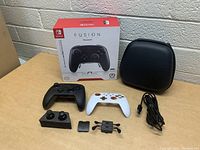 Lot contents including black and white PowerA Fusion Pro Wireless Controllers for Nintendo Switch, interchangeable accessories, charger cable, carrying case, and original box