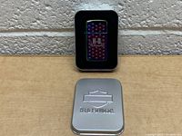 Front view of the Harley Davidson Zippo lighter inside a black foam insert within a metal case lid removed and placed nearby.