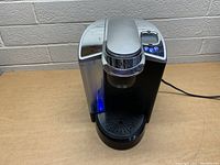 Front angled view of the Keurig coffee maker showing drip tray and control panel with buttons lit.