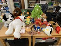 Top view of large variety of stuffed animals including dogs, dinosaurs, giraffe and others on a wooden table