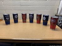 Set of 7 NHL insulated tumblers arranged in a row on a table showing team logos from left to right: Vancouver Canucks, Winnipeg Jets, Calgary Flames, Edmonton Oilers, Ottawa Senators, Toronto Maple Leafs, Montreal Canadiens.