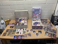 View of basketball cards spread out on a table along with two boxes containing more cards.