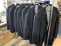 Seven black tuxedo coats hanging on a rack, showing the side profile and arrangement.