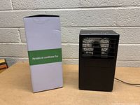Front view of the portable air conditioner fan next to its original box.
