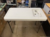Portable folding camping fish cleaning station viewed from the top showing the plastic surface and integrated drain area wrapped in plastic.