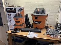 Ridgid wet/dry vacuum with box and accessories shown on table.