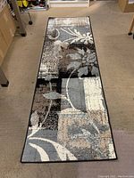 Full view of the runner rug laid out on a brown carpeted floor showing floral and geometric pattern in neutral tones.