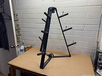 Side and angle view of the three-legged black metal stand with multiple pegs for holding plate weights