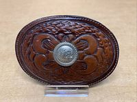 Close-up photo of a Tony Lama leather belt buckle showing intricate tooling and a silver concho center.