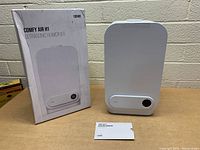 Front and side views of the white Toppin Comfy Air H1 ultrasonic humidifier with original box and user manual displayed on a table against a brick wall background.