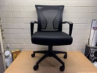 Front view of black office chair with mesh backrest, cushioned seat, armrests and caster wheels.