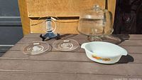 Photo showing three etched glass plates including a displayed central piece with stand and Fire King casserole dish in foreground with large cake pedestal in background.