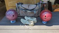 Two vintage bowling balls placed on small containers, white Brunswick bowling shoes in front of a gray NIKE bowling bag.