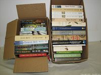 Two boxes filled with over 20 assorted used books by various authors, visible titles include Alice Munro, Lee Child, Danielle Steel, Chris Hadfield, and others.