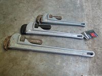 Photo of three pipe wrenches laid side by side on concrete floor, showing overall condition and brand names.
