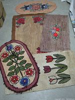Five antique hooked rugs with different floral patterns laid out on a concrete floor, showing condition and sizes.