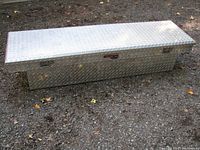 Front view of aluminum truck toolbox showing diamond plate texture, latch handles on ends, and TrailFX label on front.
