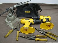 All items arranged together showing the two cordless drills, three tin snips, Pana Vice, and carry bag on a gray surface.
