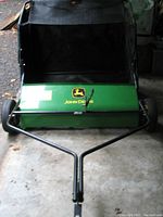 Front view showing green housing, black bag and tubular steel frame with John Deere logo
