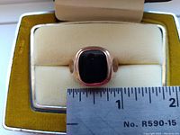 Front view of the men's 10K gold ring showing the dark center stone and measuring tape indicating size.