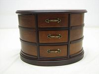 Front view of closed oval jewellery box showing three drawers with ornate brass handles and smooth walnut finish.