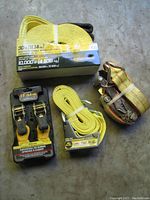Overview of all straps and tie downs included in the lot, showing new sealed packaging and metal ratchets.